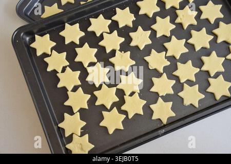 Frisch geformte Sternkekse, die auf einem Backblech angeordnet sind und in den Ofen gestellt werden können. Perfekt zum Backen im Urlaub, hausgemachte Leckereien, festliche Desserts, Stockfoto