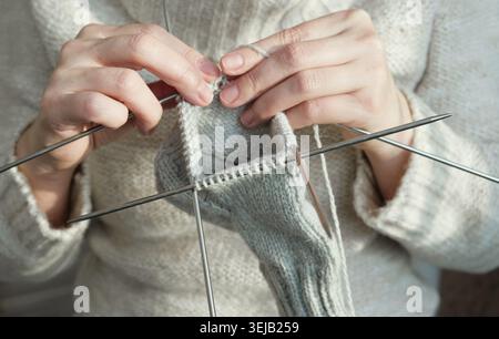 Gemütliche Strickfrau in gestricktem warmen Pullover genießt Strickarbeit zu Hause im gemütlichen Winter. Nahaufnahme Stockfoto