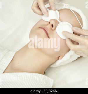 Junge kaukasische Frau, die in entspannter Umgebung mit Augenpolstern und Handschuhen eine Spa-Gesichtsbehandlung erhält Stockfoto