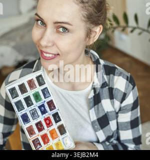 Junge kaukasische Künstlerin mit Aquarellpalette in ungezwungenem Studio-Setting Stockfoto