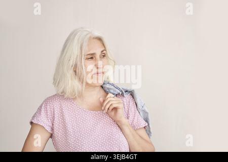 Reife weiße Frau mit grauen Haaren in rosafarbenem Polka-Dot-Shirt mit Jeansjacke Stockfoto