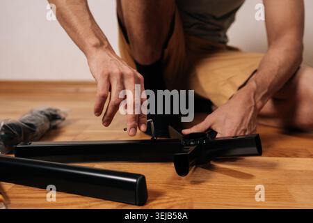 Meister, der neue Bürostuhlmöbel zusammenbaut, vorsichtig mit inbusschlüssel die Beine an der zentralen Basis befestigen, während er zu Hause auf dem Holzboden kniet Stockfoto