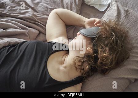 Kaukasische junge Frau schläft friedlich im Bett mit Augenmaske und entspanntem Ausdruck Stockfoto