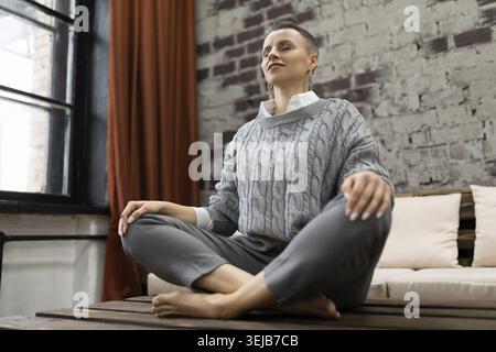 Reife Frau sitzt zu Hause auf dem Tisch in Yoga-Pose entspannend Stockfoto