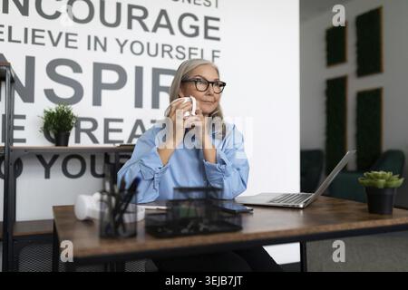 Erwachsene starke unabhängige Frau, die im Büro sitzt und eine Tasse Tee in den Händen hält Stockfoto