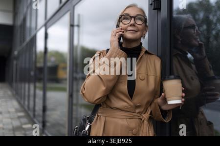 Eine ältere Geschäftsfrau geht zur Arbeit und spricht mit einem Handy Stockfoto