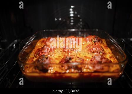 Hausgemachte Fleischbällchen, die in einer lebendigen Tomatensauce in einer klaren Auflaufform aus Glas köcheln und in einem warmen Ofen rösten und eine köstliche culina präsentieren Stockfoto