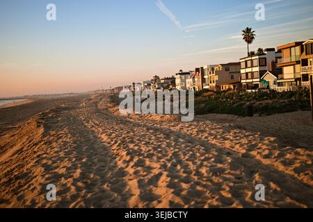 Strandhäuser erstrecken sich entlang der Sandküste in Sunset Beach, Kalifornien, unter sanftem Nachmittagslicht und einem ruhigen blauen Himmel. Stockfoto