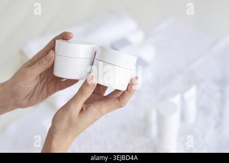 Hände halten Hautpflegegläser vor weichem Hintergrund im Spa-Setting Stockfoto