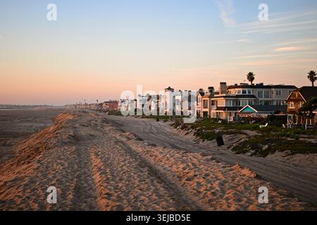 Strandhäuser erstrecken sich entlang der Sandküste in Sunset Beach, Kalifornien, unter sanftem Nachmittagslicht und einem ruhigen blauen Himmel. Stockfoto