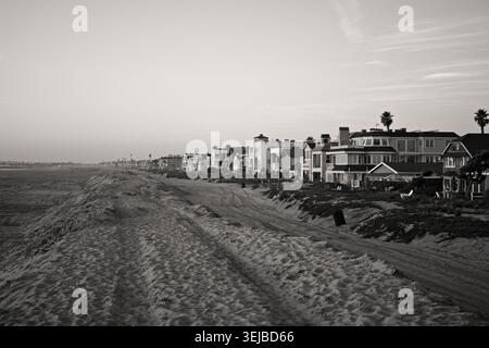 Strandhäuser erstrecken sich entlang der Sandküste in Sunset Beach, Kalifornien, unter sanftem Nachmittagslicht und einem ruhigen blauen Himmel. Stockfoto