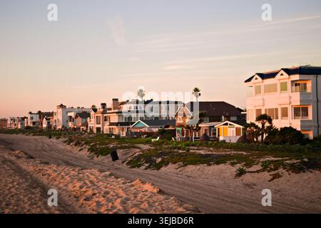 Strandhäuser erstrecken sich entlang der Sandküste in Sunset Beach, Kalifornien, unter sanftem Nachmittagslicht und einem ruhigen blauen Himmel. Stockfoto