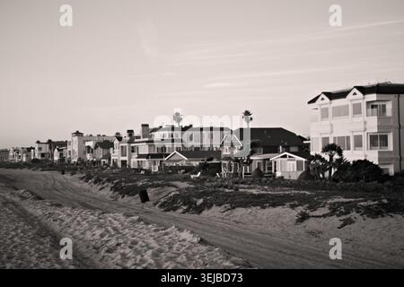 Strandhäuser erstrecken sich entlang der Sandküste in Sunset Beach, Kalifornien, unter sanftem Nachmittagslicht und einem ruhigen blauen Himmel. Stockfoto