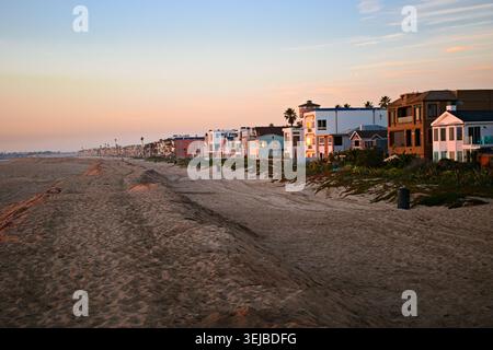 Strandhäuser erstrecken sich entlang der Sandküste in Sunset Beach, Kalifornien, unter sanftem Nachmittagslicht und einem ruhigen blauen Himmel. Stockfoto