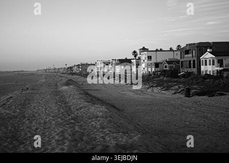 Strandhäuser erstrecken sich entlang der Sandküste in Sunset Beach, Kalifornien, unter sanftem Nachmittagslicht und einem ruhigen blauen Himmel. Stockfoto