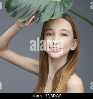 Junge Weibchen mit langen Haaren, die unter Monstera lächeln Stockfoto