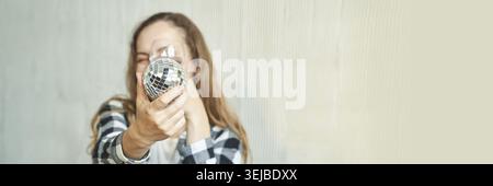Lächelnde weiße junge Frau mit glänzender Disco-Kugel in lässigem Karohemd Stockfoto