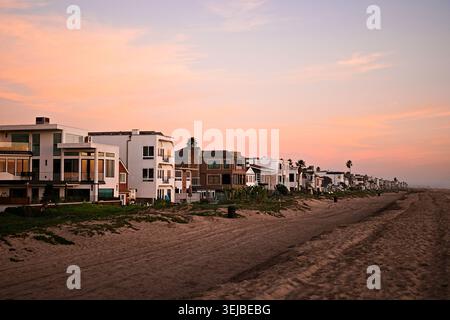 Strandhäuser erstrecken sich entlang der Sandküste in Sunset Beach, Kalifornien, unter sanftem Nachmittagslicht und einem ruhigen blauen Himmel. Stockfoto