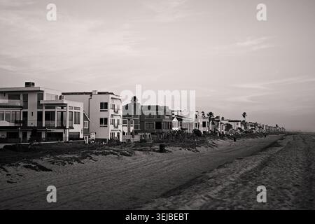 Strandhäuser erstrecken sich entlang der Sandküste in Sunset Beach, Kalifornien, unter sanftem Nachmittagslicht und einem ruhigen blauen Himmel. Stockfoto