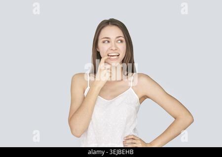 Junge Weibchen in weißer Spitze posiert nachdenklich vor hellgrauem Hintergrund Stockfoto