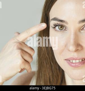 Nahaufnahme einer erwachsenen kaukasischen Frau, die mit fokussiertem Ausdruck auf die Stirn zeigt Stockfoto