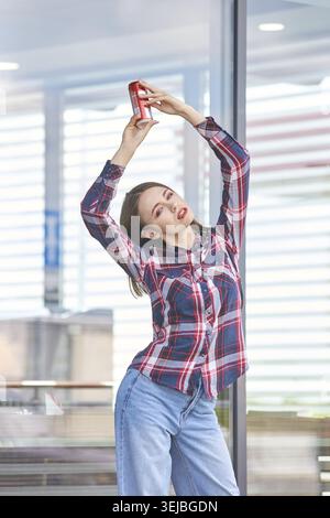 Junge weiße Frau in kariertem Hemd, die rot hält, kann sich im Freien spielerisch posieren Stockfoto