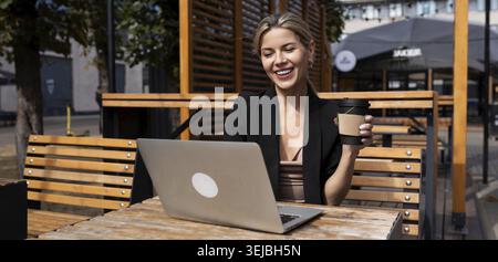 Junge erfolgreiche Geschäftsfrau, die mit Laptop arbeitet und draußen Kaffee trinkt Stockfoto