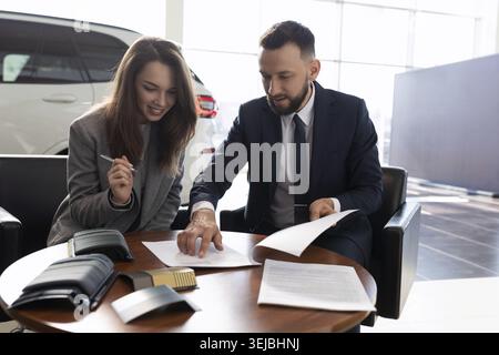 Die junge Frau kauft ein neues Auto in einem Autohändler und unterzeichnet Dokumente Stockfoto