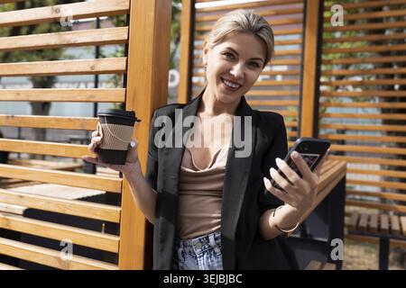 Porträt einer erfolgreichen Geschäftsfrau mittleren Alters in einem Stadtcafé mit Telefon und einem Glas Kaffee Stockfoto