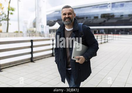 Reifer bärtiger Mann mit Laptop, der draußen läuft Stockfoto