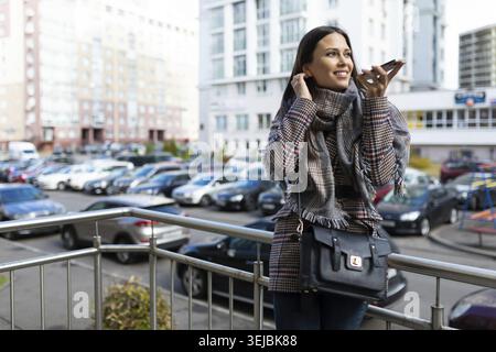 Junge, schöne Frau, die draußen auf dem Freisprechtelefon spricht Stockfoto