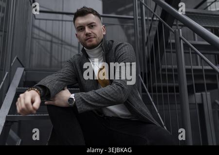 Stilvoller, eleganter junger Mann aus dem kaukasus, der draußen auf schwarzen Stufen sitzt Stockfoto