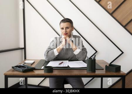 Nachdenkliche, reife Geschäftsfrau sitzt hinter Dokumenten im Büro Stockfoto
