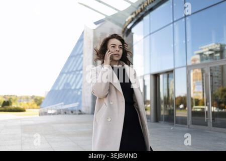 Eine Geschäftsfrau eilt zu einem Meeting im Hintergrund eines Geschäftsgebäudes und spricht am Telefon Stockfoto