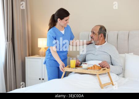 Die Pflegekraft frühstückt einem älteren Mann zu Hause im Bett Stockfoto