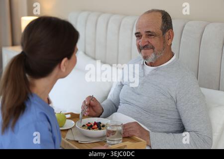 Die Pflegekraft frühstückt einem älteren Mann zu Hause im Bett Stockfoto