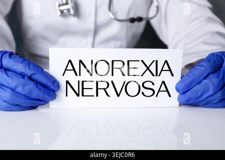 Doktor hält Karte mit den Worten Anorexia nervosa am Tisch, Nahaufnahme Stockfoto