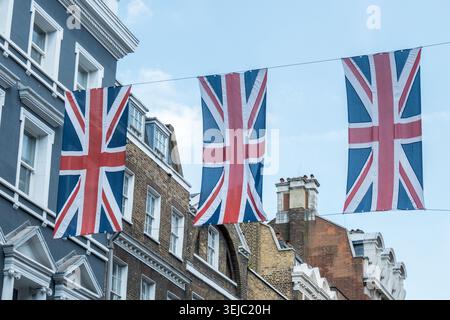 Drei große Union Jack Flaggen hängen an Drähten über einer traditionellen Londoner Straße mit georgianischen und viktorianischen Gebäuden vor einem blauen Himmel Stockfoto