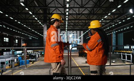 Verschiedene Mitarbeiter beaufsichtigen das autonome Roboterarmsystem auf Laptop-Software im Industrielager. Ingenieure, die High-Tech-Robotik für große Fertigungsprozesse in der Industriehalle sicherstellen. Stockfoto
