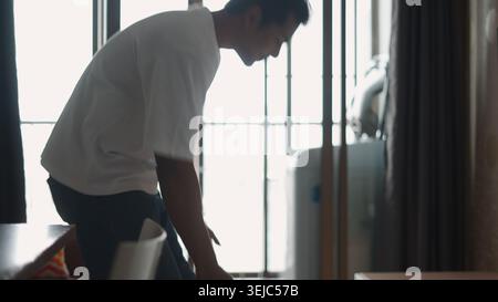 Junger Mann, der sich in einem hellen Haus bändigt, tägliche Aufgaben oder Aktivitäten erledigt Stockfoto