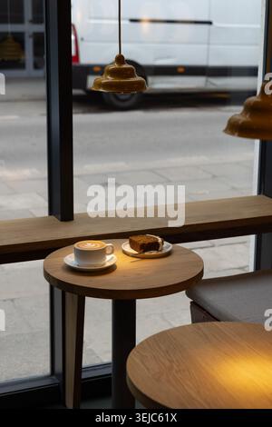 Kaffee und Kuchen in einem modernen Café-Interieur am Fenster, Fernarbeit Stockfoto