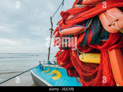 Aus nächster Nähe sehen Sie lebendige rote Fischernetze mit farbenfrohen Plastikwagen, die auf einem traditionellen Sri-lankischen Auslegerboot am Sandstrand am Meer geparkt sind Stockfoto