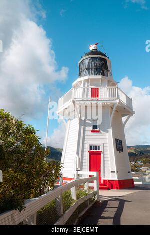 Akaroa, Neuseeland: Senkrechter Blick auf den historischen Leuchtturm der Stadt, den berühmten weißen achteckigen Holzturm mit roter Tür an einem frischen Frühlingstag, den lebendigen Himmel Stockfoto