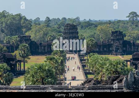 Eine erhöhte Ansicht blickt die lange Steinmole von Angkor Wat hinunter, mit Touristen und Palmen, die den Weg zum westlichen Gopura in Kambodscha säumen Stockfoto