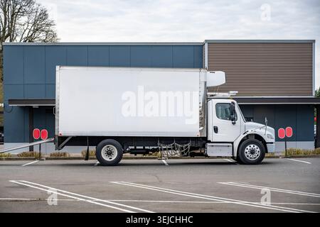 Kompakter, kompakter Auflieger mit weißem Tagfahrerhaus für industrielle Zwecke mit langem Kühlkastenanhänger und Hebebühne, die auf dem Parkplatz steht Stockfoto