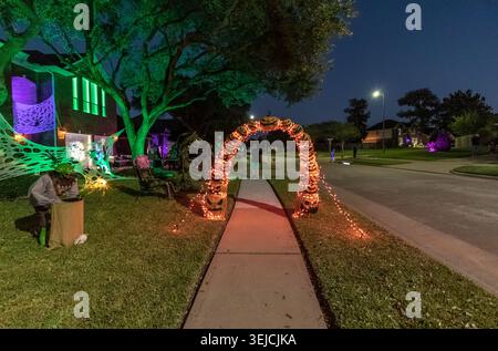 Beleuchteter Jack-o'-Lantern-Bogen mit orangefarbenen und lila Lichterketten über einem für die Halloween-Nacht dekorierten Bürgersteig in einer texanischen Vorstadt Stockfoto