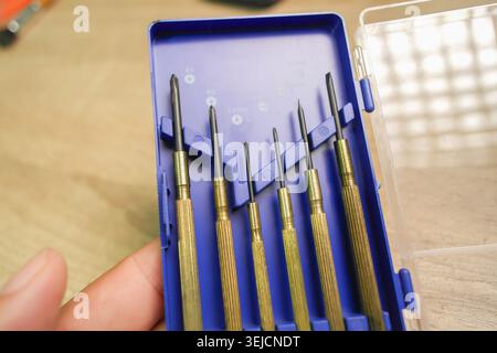 Eine Hand, die ein offenes blaues Kunststoffgehäuse mit einem Satz Präzisionsschraubendreher aus Messing hält, perfekt für Reparaturen an Mikroelektronik, Uhrmacherei und kleine Stockfoto