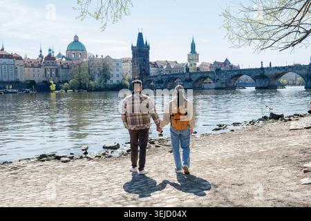 Ein Paar schlendert Hand in Hand entlang der malerischen Moldau in Prag und genießt einen sonnigen Frühlingstag. Stockfoto