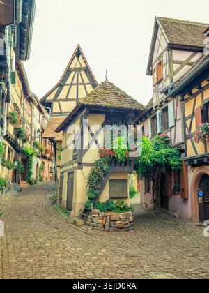 Eguisheim, Frankreich - 13.08.2023: Malerische elsässische Dorfstraße mit traditionellen Fachwerkhäusern und üppigen Fensterblumenkästen Stockfoto