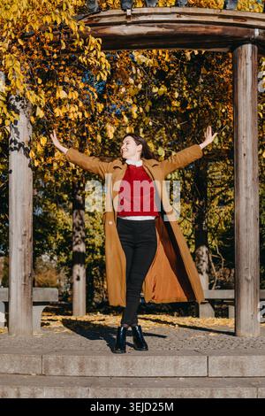 Frau lächelt, während sie draußen in der Nähe von Bäumen mit Herbstlaub läuft. Ausdruck von purem Glück, positiver geistiger Gesundheit, Achtsamkeit im täglichen Leben Stockfoto